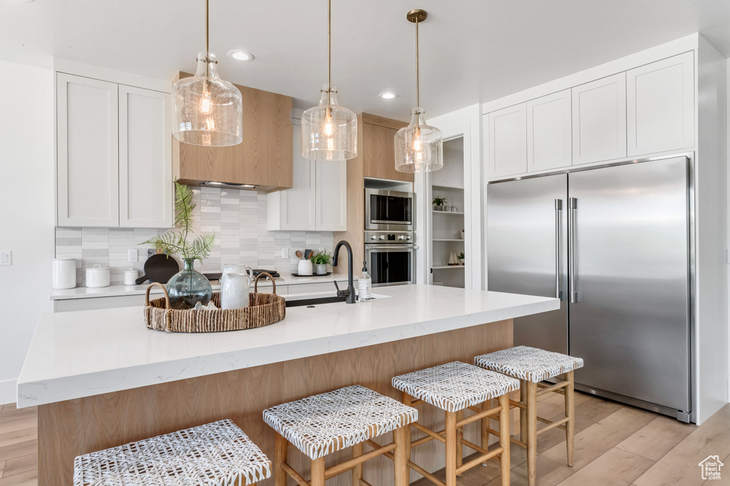 Kitchen featuring white cabinets, backsplash, built in appliances, and light hardwood / wood-style floors