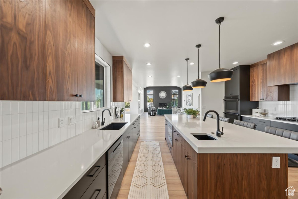 Kitchen with a kitchen island with sink, sink, hanging light fixtures, light hardwood / wood-style floors, and tasteful backsplash