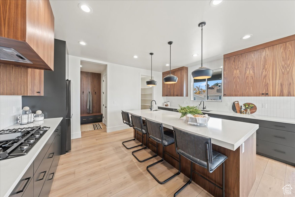 Kitchen featuring backsplash, a kitchen bar, light hardwood / wood-style flooring, wall chimney exhaust hood, and pendant lighting