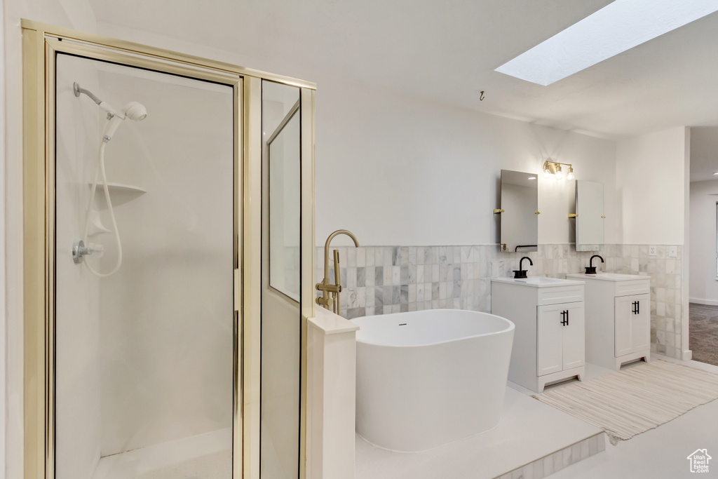Bathroom featuring a skylight, vanity with extensive cabinet space, plus walk in shower, and tile walls