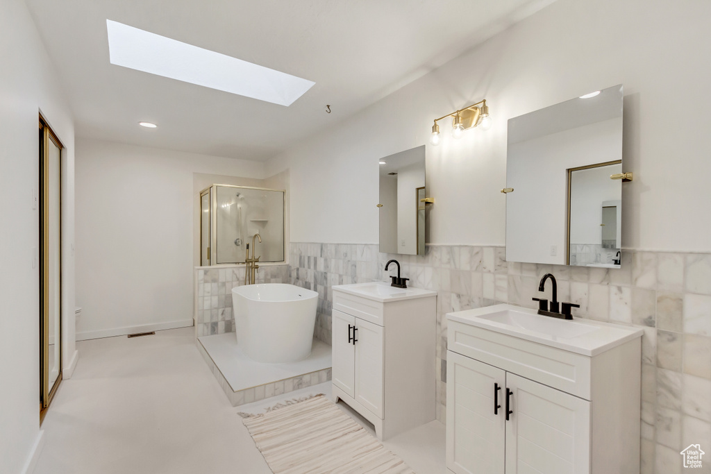 Bathroom featuring a skylight, tile walls, dual sinks, tile flooring, and vanity with extensive cabinet space