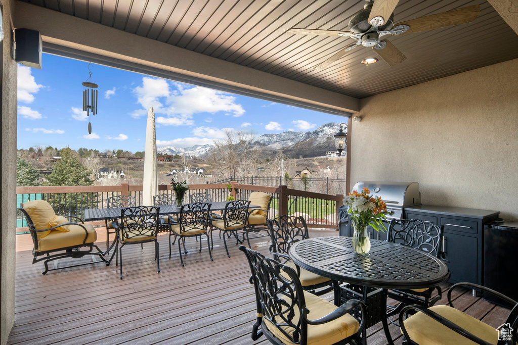 Wooden terrace featuring grilling area, an outdoor kitchen, a mountain view, and ceiling fan