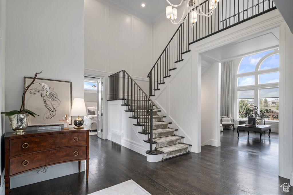 Entrance foyer featuring a towering ceiling, a chandelier, crown molding, and dark hardwood / wood-style flooring