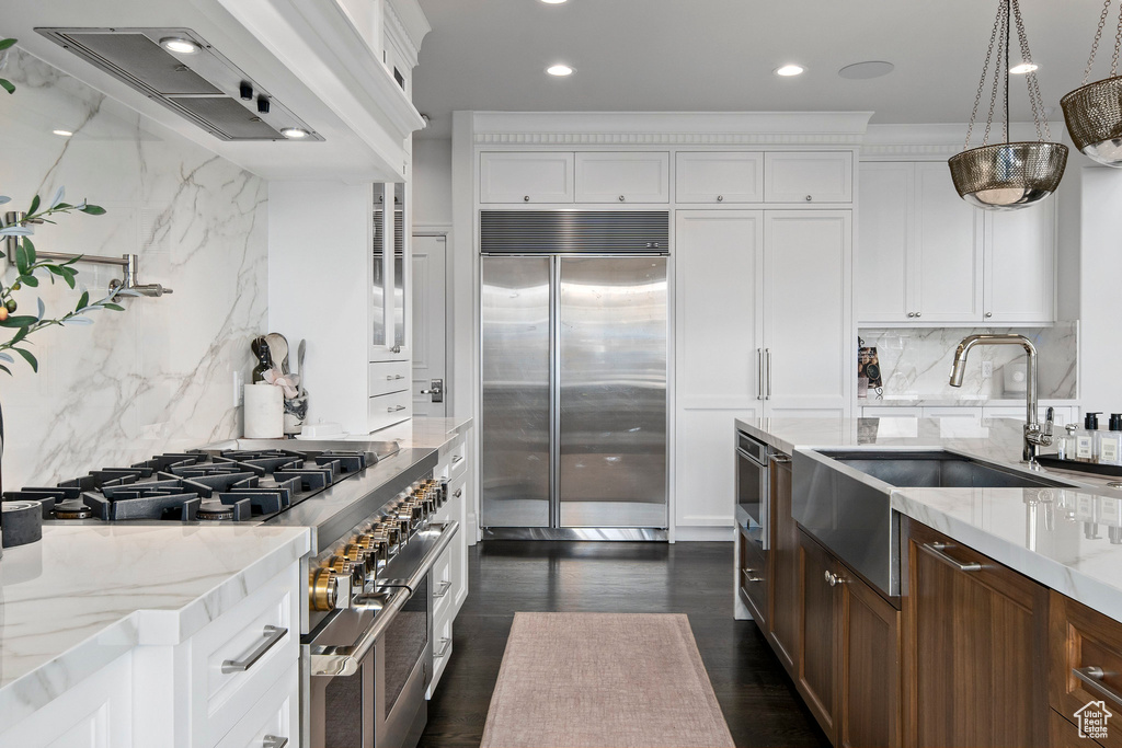 Kitchen with pendant lighting, light stone counters, white cabinets, backsplash, and high quality appliances