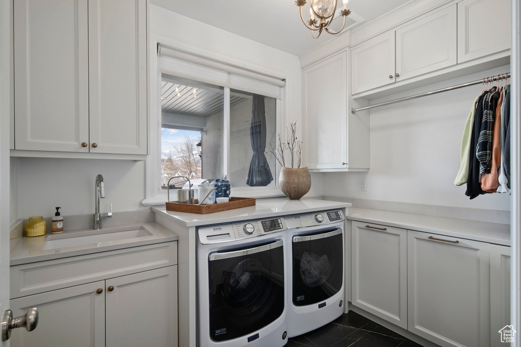 Clothes washing area featuring dark tile floors, sink, a notable chandelier, cabinets, and separate washer and dryer