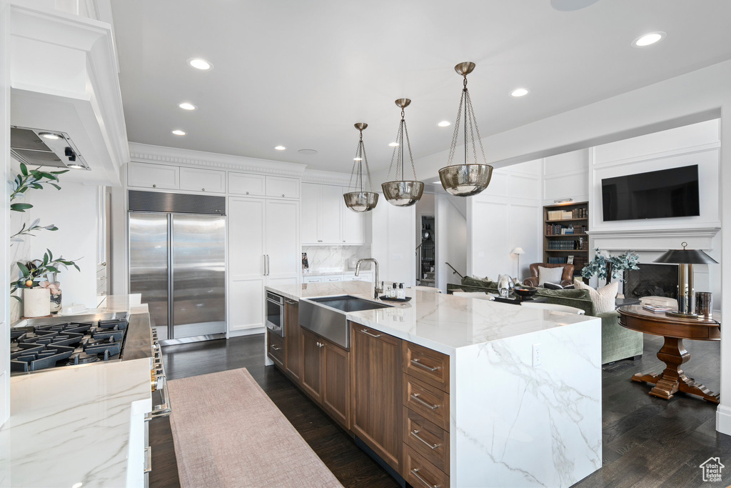 Kitchen featuring decorative light fixtures, a kitchen island with sink, built in fridge, white cabinets, and dark hardwood / wood-style flooring