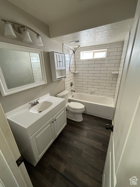 Full bathroom with wood-type flooring, tiled shower / bath, a textured ceiling, vanity with extensive cabinet space, and toilet