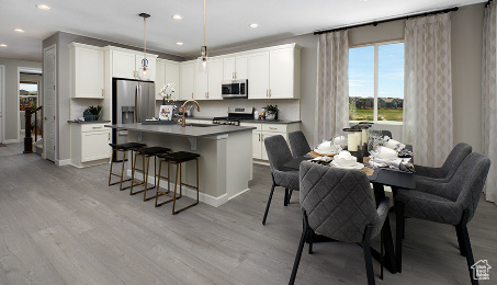 Kitchen with a breakfast bar area, white cabinetry, appliances with stainless steel finishes, and light hardwood / wood-style flooring