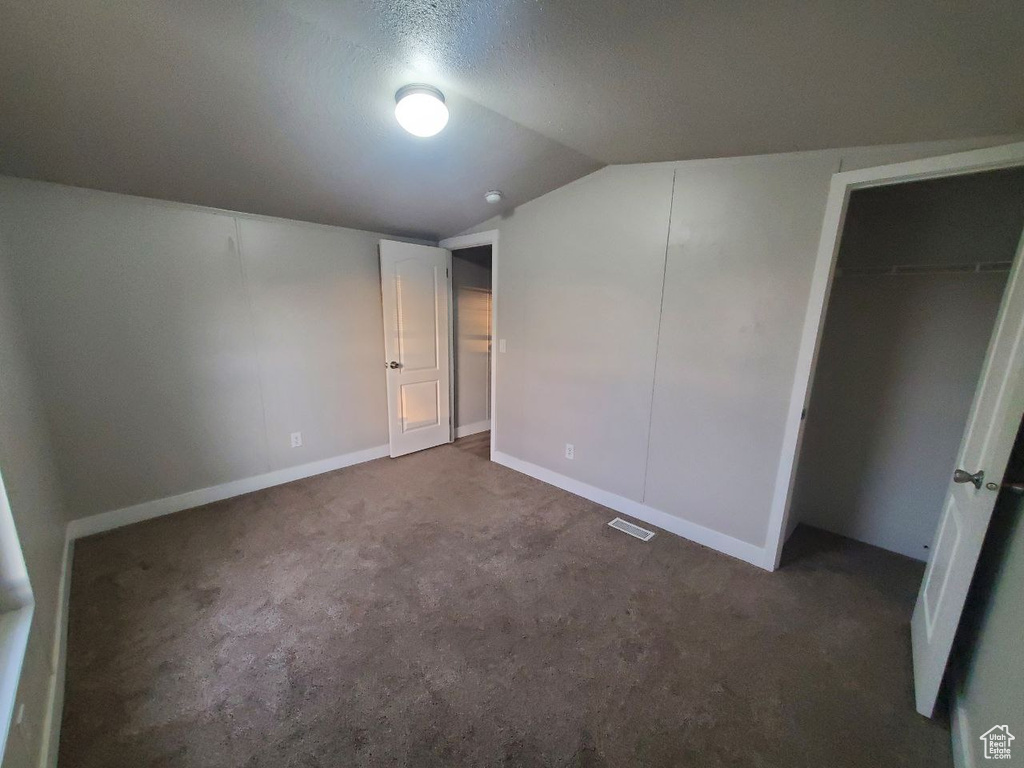 Unfurnished bedroom featuring lofted ceiling, a closet, dark colored carpet, and a textured ceiling