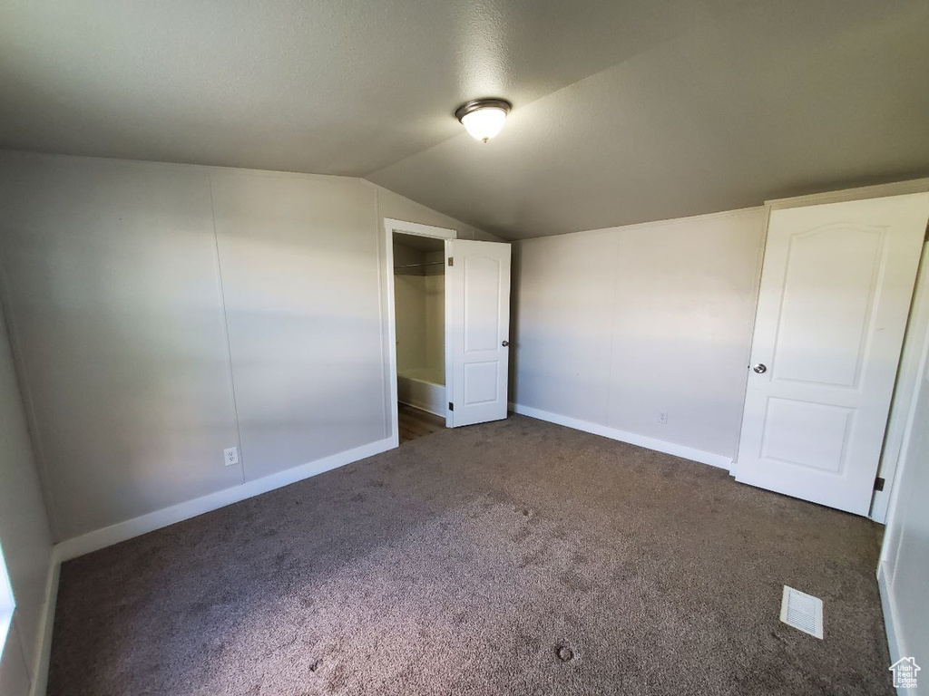 Unfurnished bedroom with lofted ceiling, dark carpet, and a closet