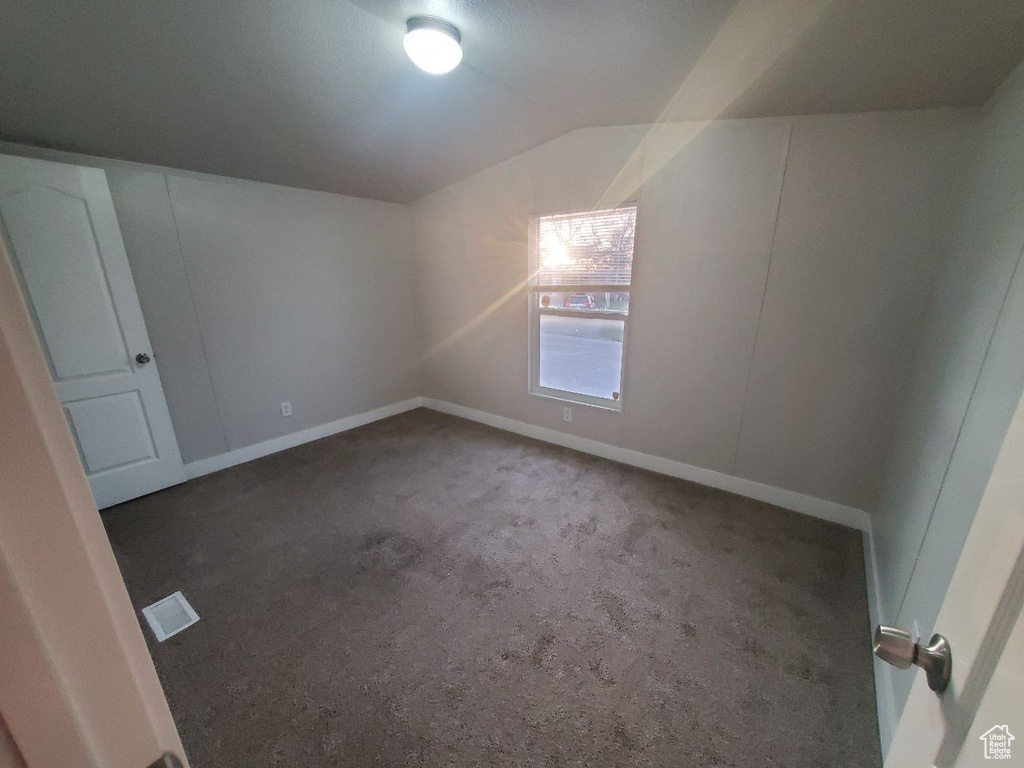 Empty room with dark colored carpet and lofted ceiling