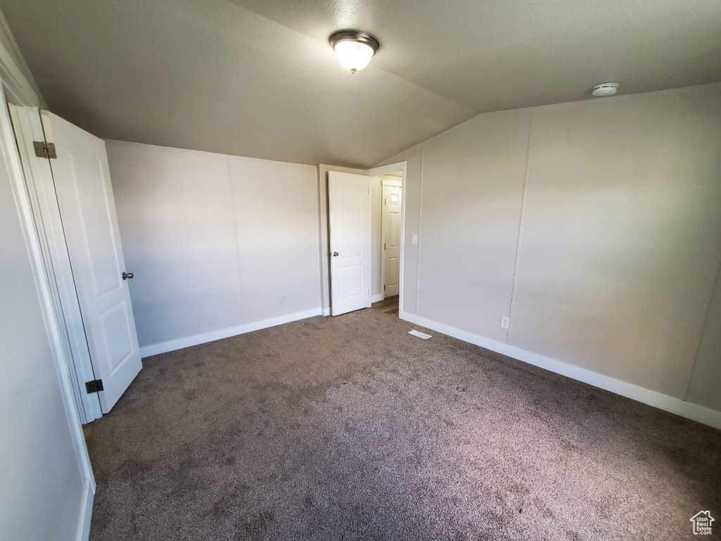 Unfurnished bedroom with lofted ceiling and dark colored carpet