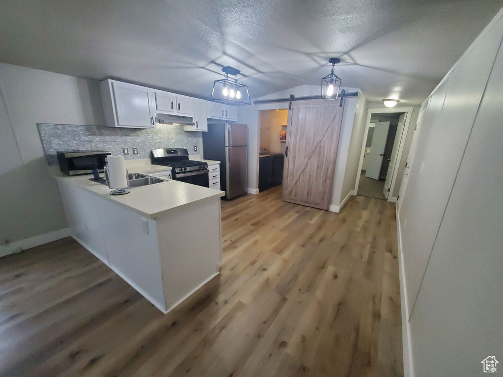 Kitchen with a barn door, appliances with stainless steel finishes, light wood-type flooring, white cabinets, and pendant lighting