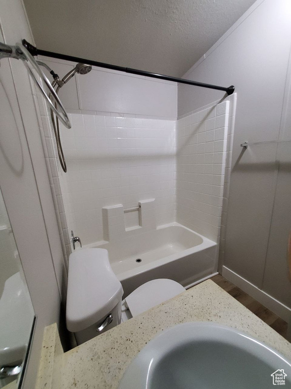 Bathroom with toilet, hardwood / wood-style floors, tiled shower / bath combo, and a textured ceiling