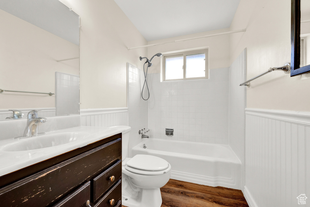 Full bathroom featuring tiled shower / bath combo, wood-type flooring, vanity with extensive cabinet space, and toilet