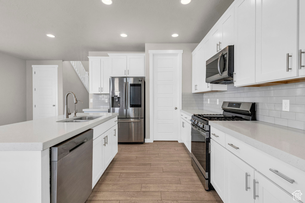 Kitchen featuring light hardwood / wood-style floors, white cabinetry, backsplash, and stainless steel appliances