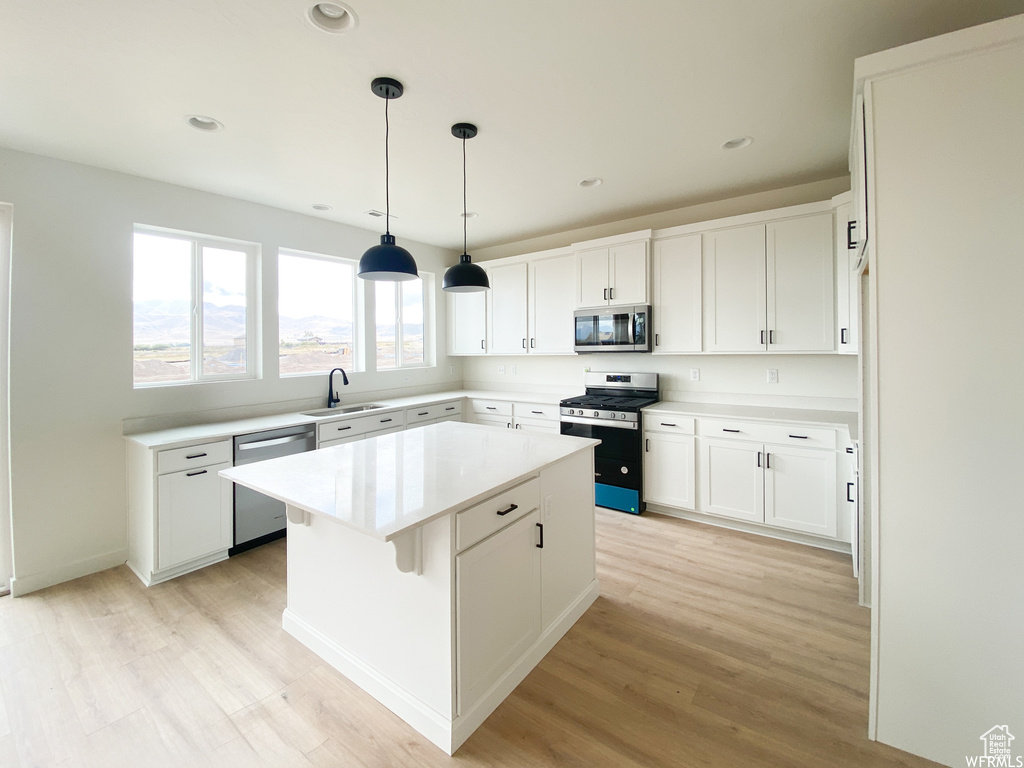 Kitchen featuring light wood-type flooring, stainless steel appliances, a kitchen island, and white cabinetry