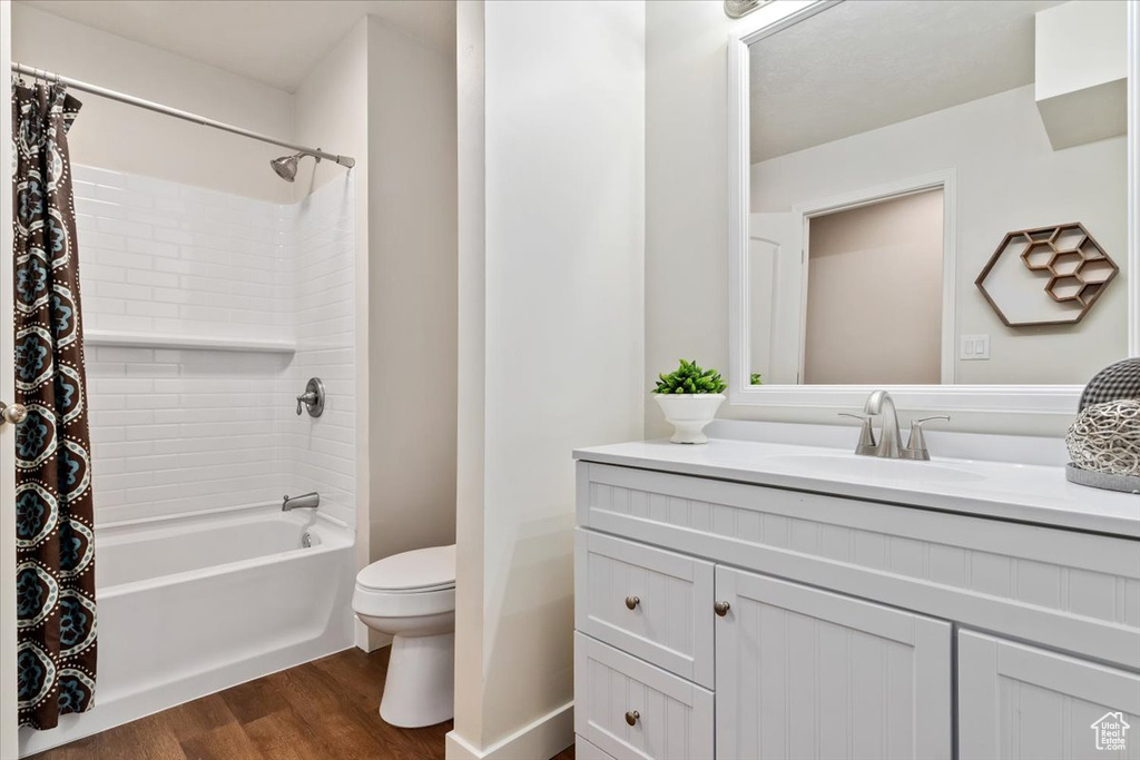 Full bathroom featuring toilet, shower / bath combo, vanity with extensive cabinet space, and hardwood / wood-style flooring