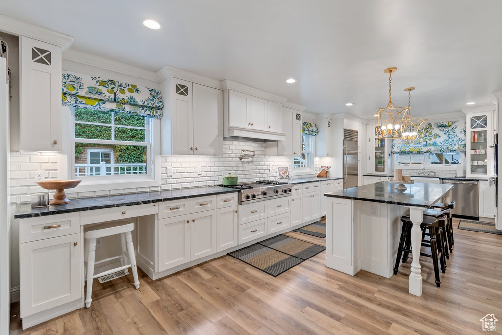 Kitchen with stainless steel appliances, a breakfast bar, tasteful backsplash, light hardwood / wood-style flooring, and white cabinets
