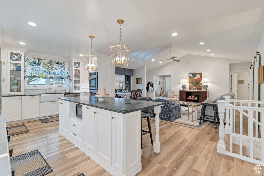 Kitchen featuring white cabinetry, ceiling fan with notable chandelier, a breakfast bar area, and light wood-type flooring