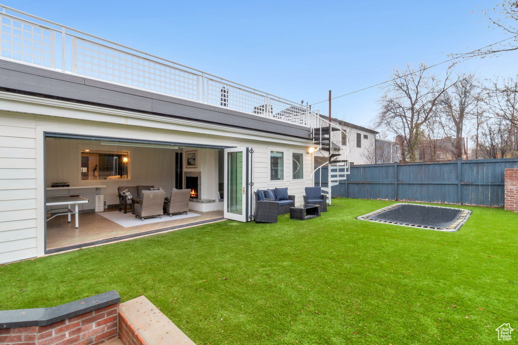 Rear view of property featuring outdoor lounge area, a trampoline, and a lawn
