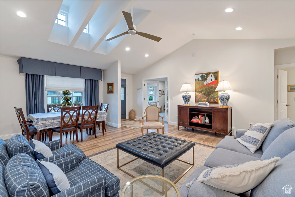 Living room featuring high vaulted ceiling, ceiling fan, a skylight, and light wood-type flooring