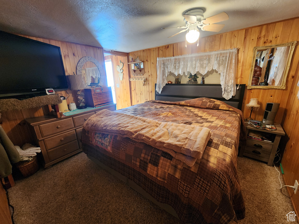 Carpeted bedroom featuring wood walls, a textured ceiling, and ceiling fan