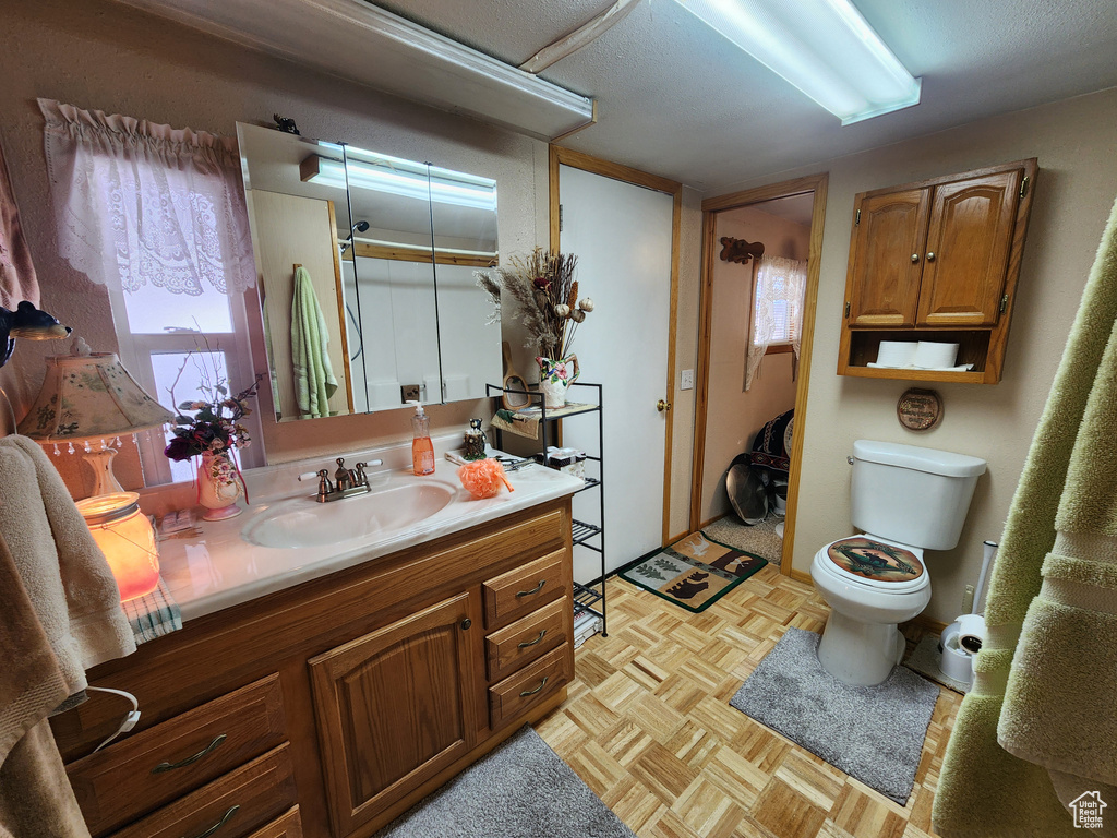 Bathroom with toilet, a textured ceiling, vanity, and parquet flooring