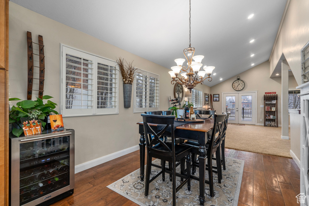 Dining space with beverage cooler, french doors, a notable chandelier, high vaulted ceiling, and dark wood-type flooring
