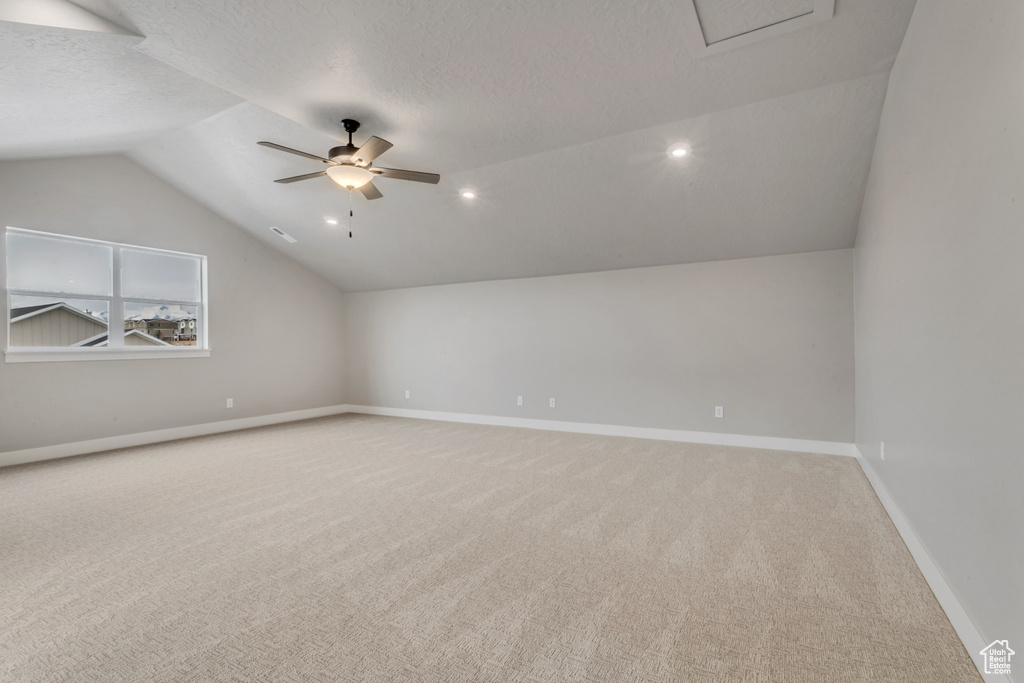 Carpeted empty room featuring vaulted ceiling, ceiling fan, and a textured ceiling