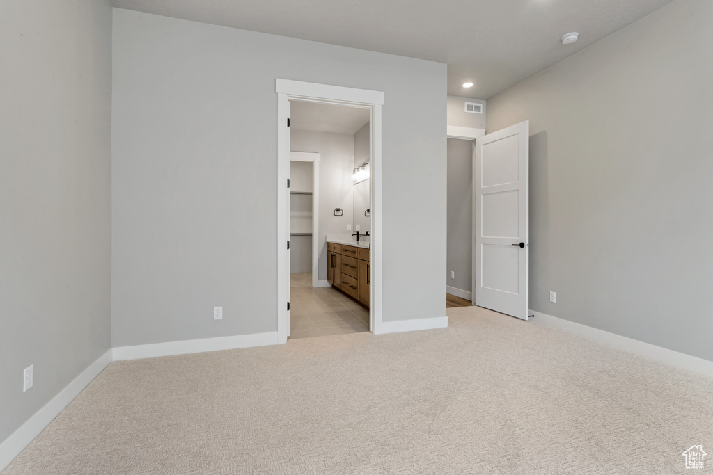 Unfurnished bedroom with light carpet, a spacious closet, and ensuite bath