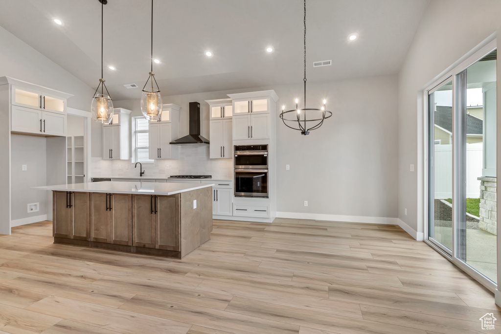 Kitchen featuring white cabinetry, wall chimney range hood, a kitchen island, tasteful backsplash, and pendant lighting