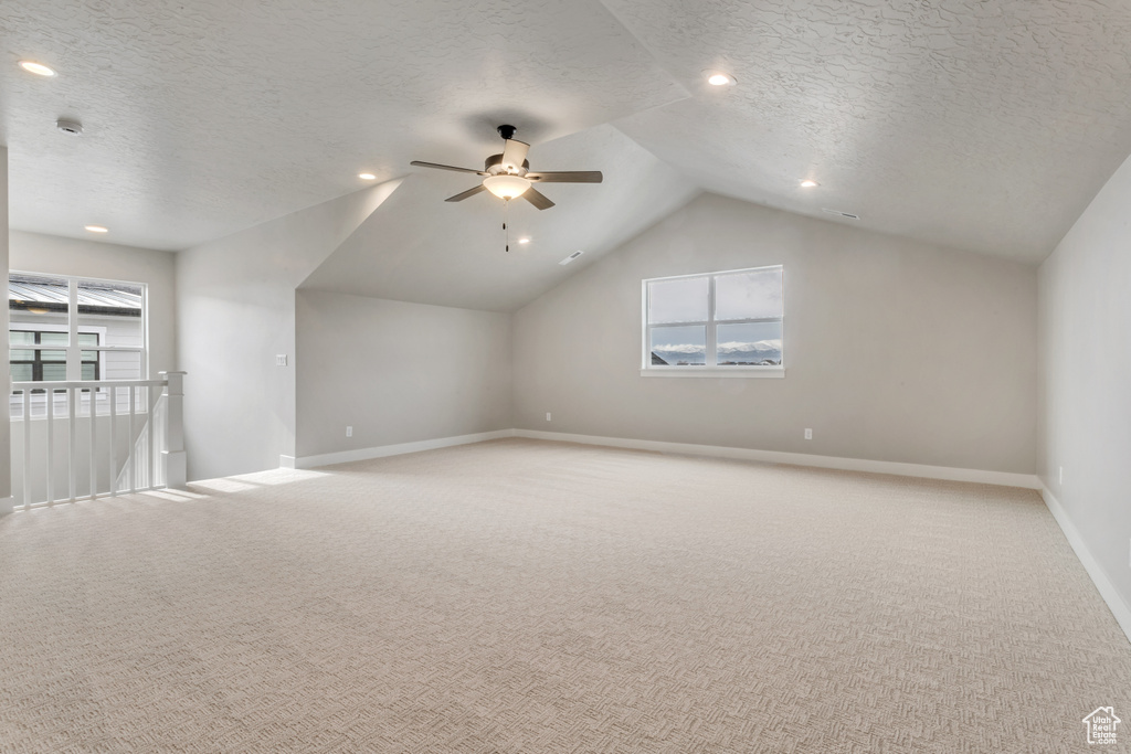 Additional living space featuring a textured ceiling, lofted ceiling, ceiling fan, and light colored carpet