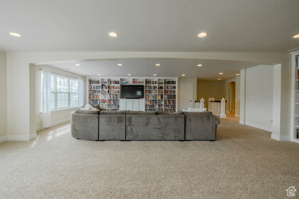 Unfurnished living room with built in shelves, light colored carpet, and a textured ceiling