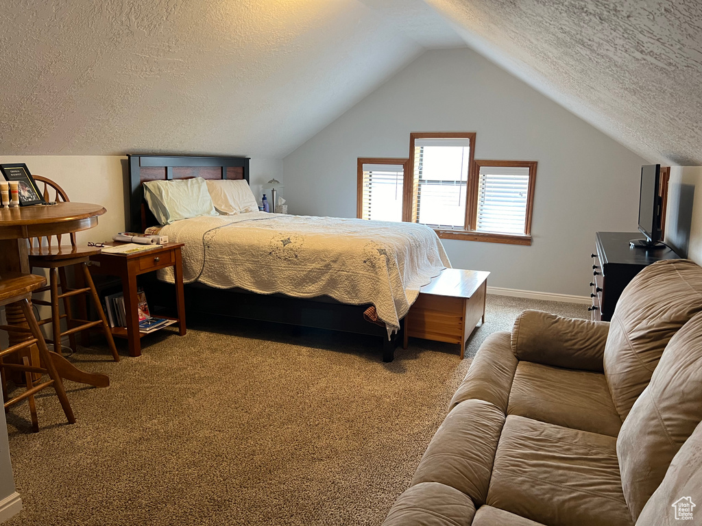 Bedroom with a textured ceiling, vaulted ceiling, and carpet