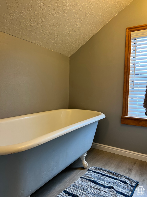Bathroom featuring hardwood / wood-style floors, a textured ceiling, a washtub, and vaulted ceiling
