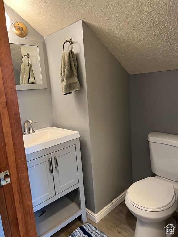 Bathroom featuring toilet, hardwood / wood-style flooring, a textured ceiling, vanity, and lofted ceiling