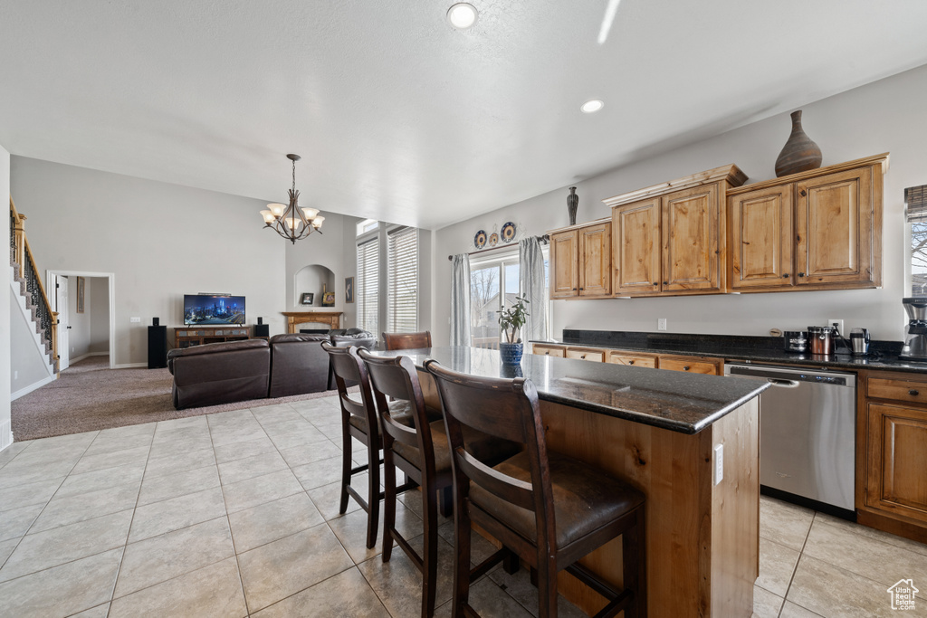 Kitchen featuring dark stone countertops, stainless steel dishwasher, a breakfast bar area, a notable chandelier, and a center island