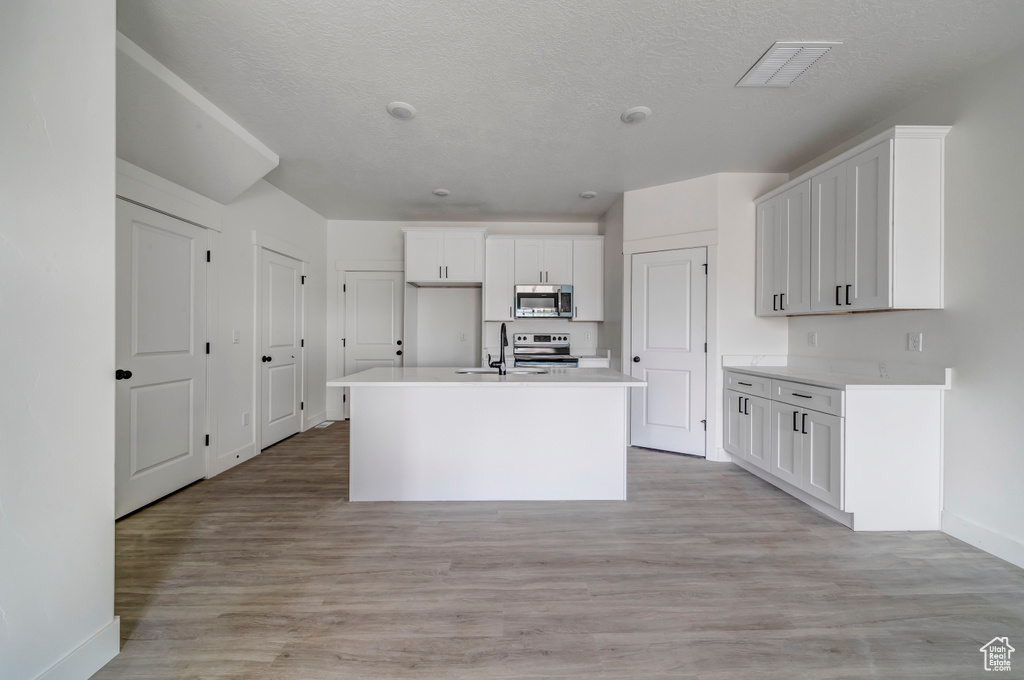 Kitchen with an island with sink, sink, white cabinets, light hardwood / wood-style flooring, and range