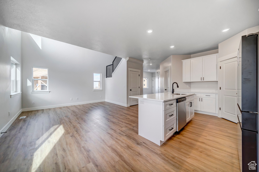 Kitchen with stainless steel dishwasher, light hardwood / wood-style flooring, sink, white cabinets, and black fridge