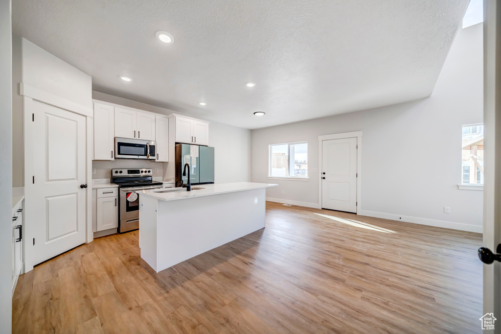 Kitchen featuring white cabinets, light hardwood / wood-style flooring, stainless steel appliances, and a kitchen island with sink