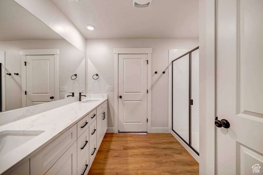 Bathroom with double vanity, a shower with shower door, and hardwood / wood-style floors