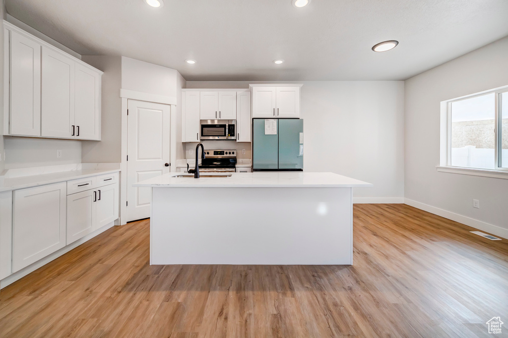 Kitchen with sink, light wood-type flooring, stainless steel appliances, a center island with sink, and white cabinets