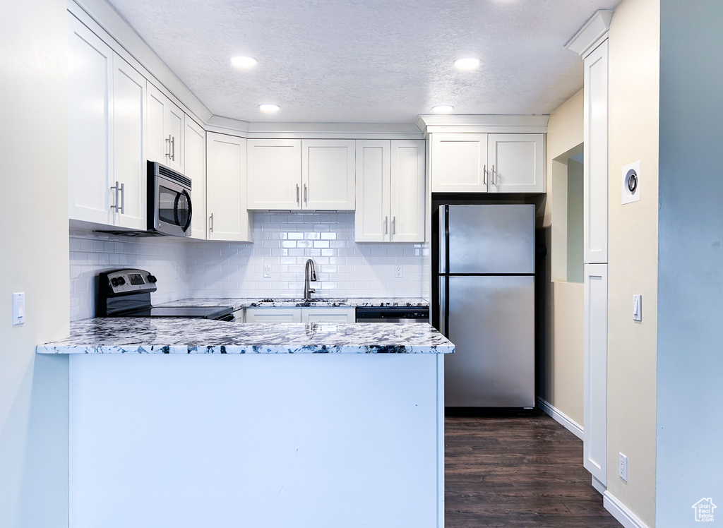 Kitchen with stainless steel appliances, light stone countertops, tasteful backsplash, white cabinetry, and dark hardwood / wood-style flooring