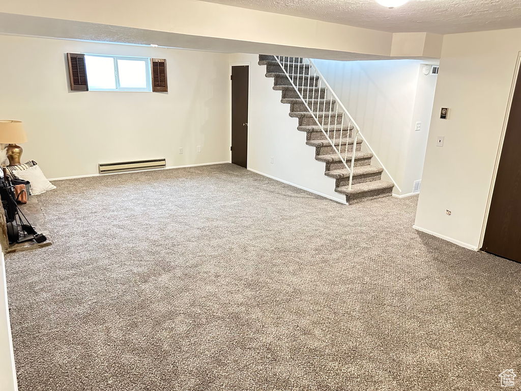 Basement with carpet flooring, a textured ceiling, and a baseboard heating unit