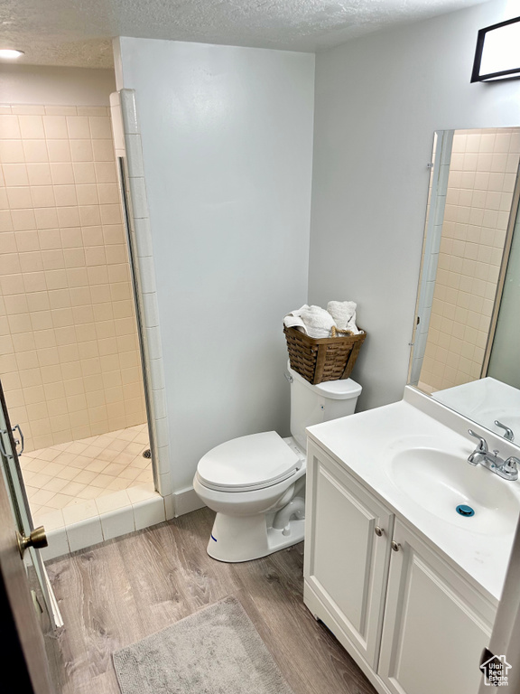 Bathroom with vanity, tiled shower, a textured ceiling, toilet, and hardwood / wood-style flooring