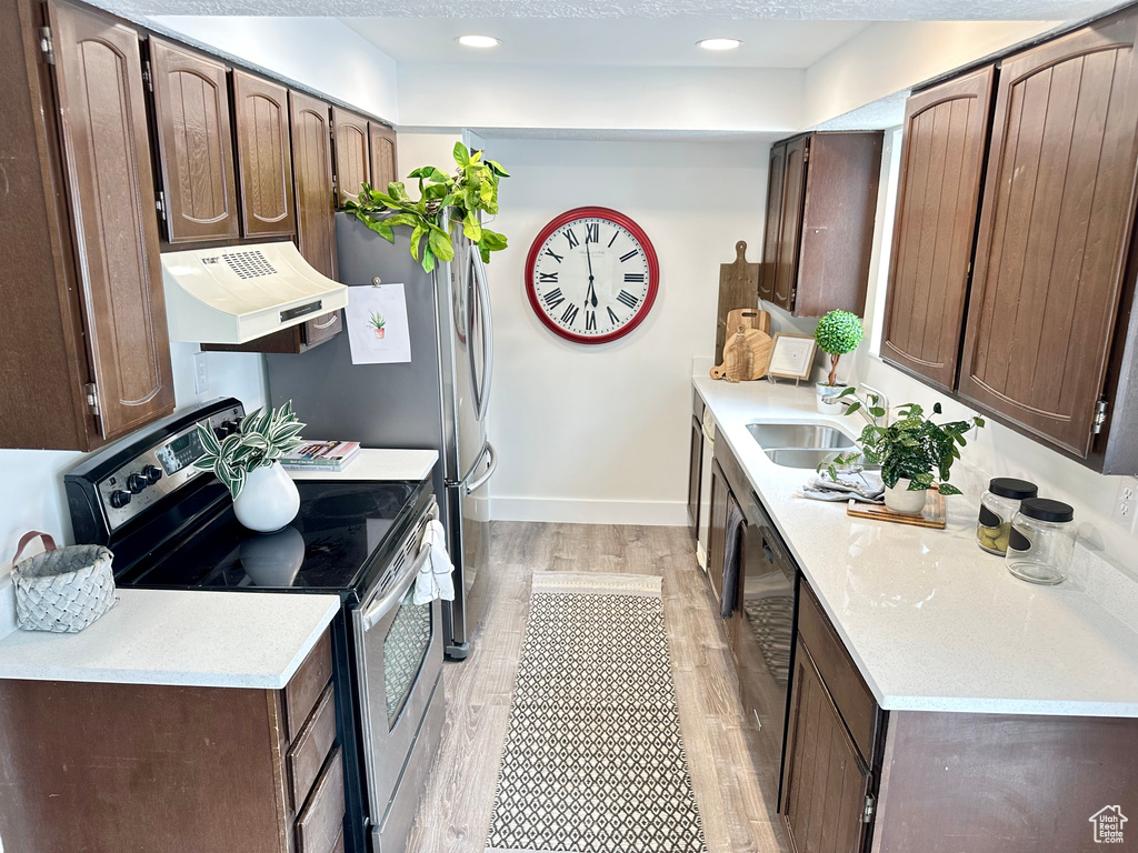 Kitchen with electric range, sink, light wood-type flooring, custom range hood, and dark brown cabinetry