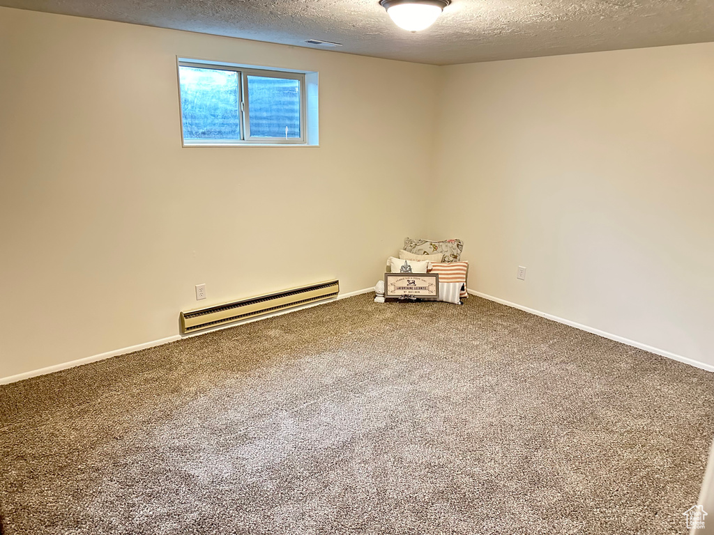 Unfurnished room featuring a textured ceiling, carpet flooring, and a baseboard radiator