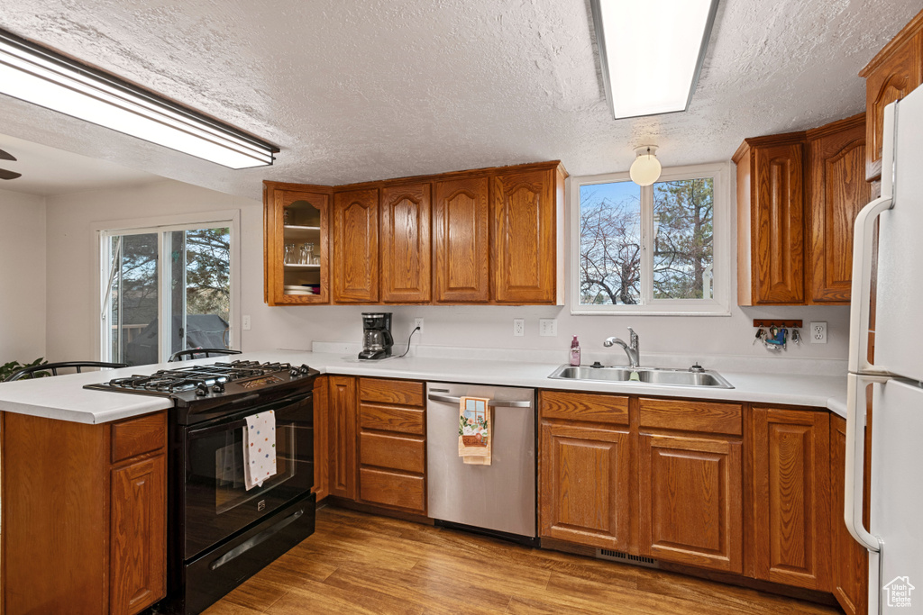 Kitchen with black gas range, white fridge, dishwasher, light wood-type flooring, and sink
