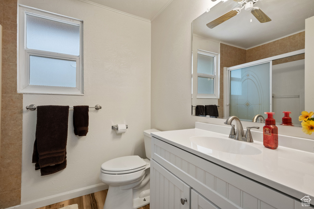 Bathroom with toilet, ceiling fan, vanity with extensive cabinet space, ornamental molding, and hardwood / wood-style flooring
